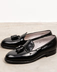 A pair of black cordovan tassel loafers with a flat welt and tassel detail, displayed against a neutral background.